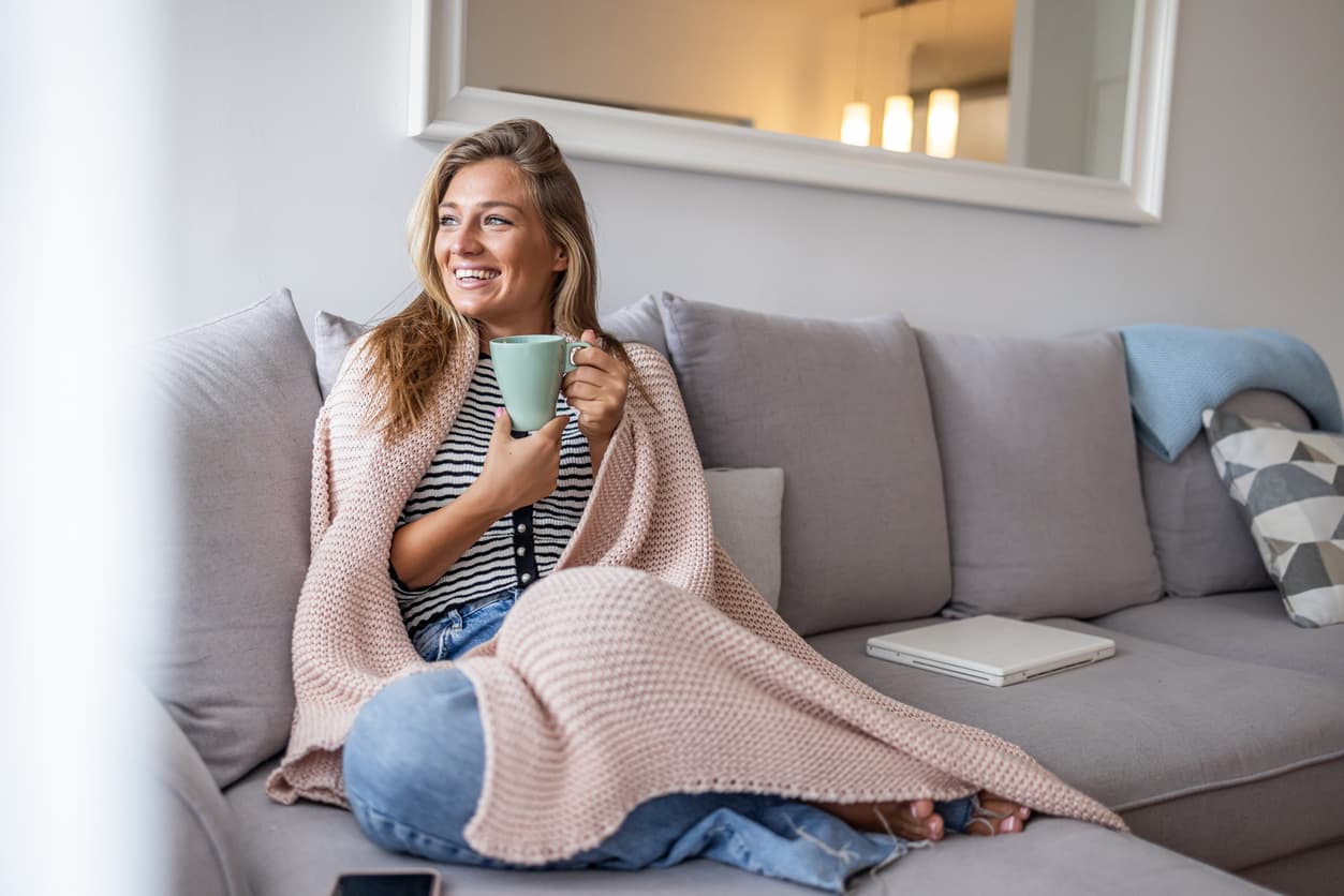 Lächelnde Frau entspannt zu Hause mit einer Tasse auf dem Sofa